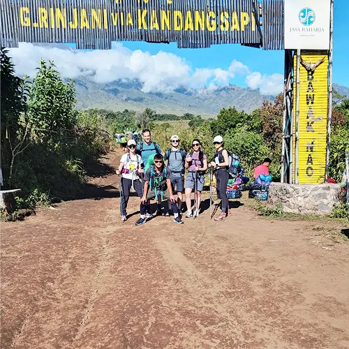 Hikers gather in front of a sign labeled kandang sampi indicating the start of their Mount Rinjani adventure Hikers gather in front of a sign labeled kandang sampi indicating the start of their Mount Rinjani adventure